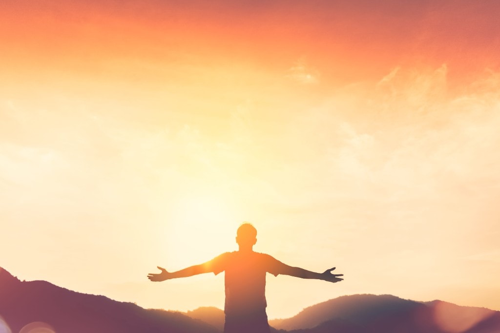 Person celebrating at sunrise over mountains